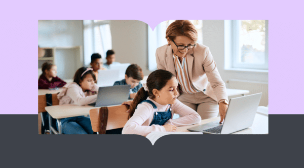 A teacher in a classroom offering one-on-one support to a student using a laptop, while other students work independently in the background.